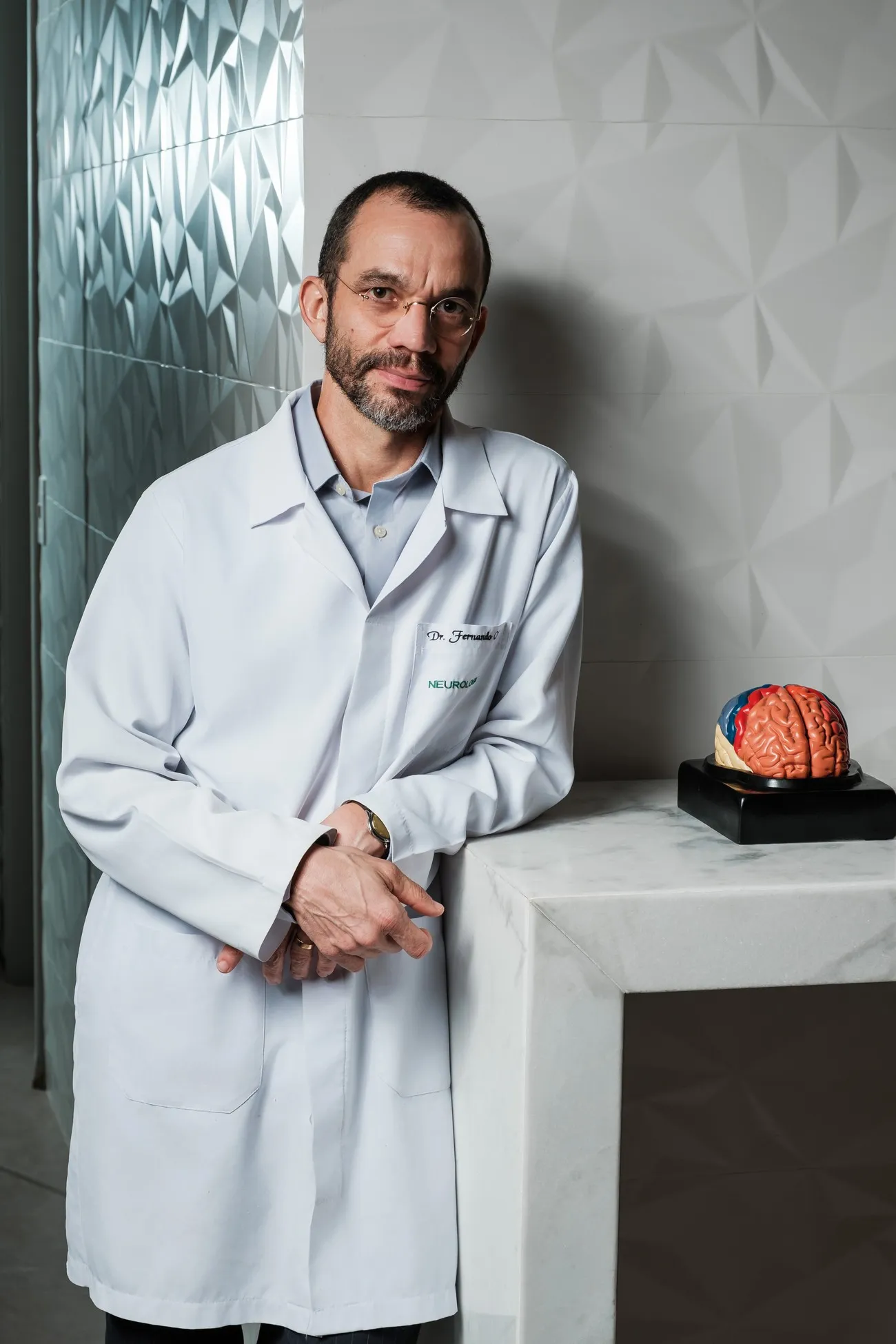 Dr. Fernando Cini Freitas de jaleco branco no consultório, ao lado de um modelo anatômico do cérebro